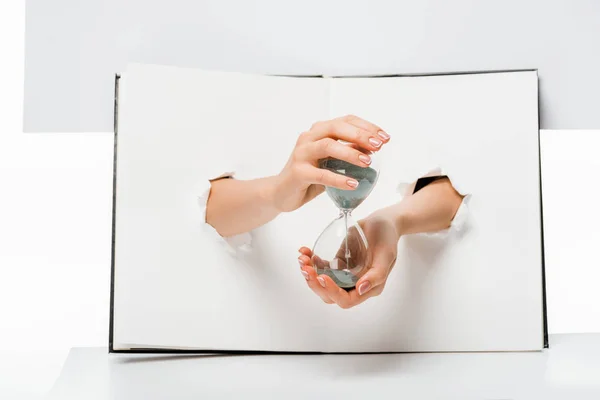 Tiro recortado de mujer sosteniendo vidrio de arena a través de agujeros en blanco - foto de stock