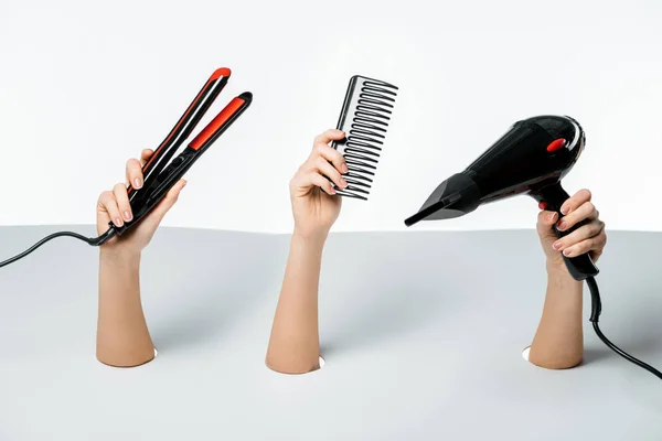 Vue partielle des mains féminines tenant des outils de coiffure à travers des trous sur blanc — Photo de stock