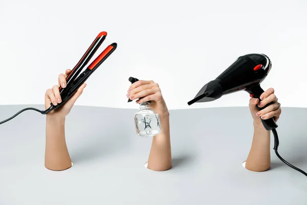 Partial view of women holding hairstyle tools through holes on white — Stock Photo