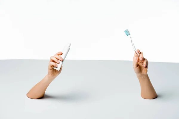 Visão parcial da mulher segurando escova de dentes e pasta de dentes através de furos no branco — Fotografia de Stock