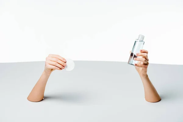 Cropped shot of woman holding cotton pad and makeup remover through holes on white — Stock Photo