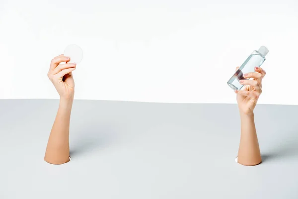 Cropped shot of woman holding cotton pad and lotion through holes on white — Stock Photo
