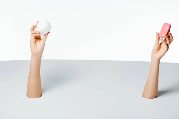 Partial view of woman holding soap and cream through holes on white — Stock Photo