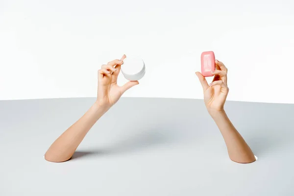 Cropped shot of woman holding soap and cream through holes on white — Stock Photo