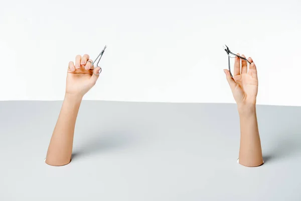 Partial view of woman holding manicure tools through holes on white — Stock Photo