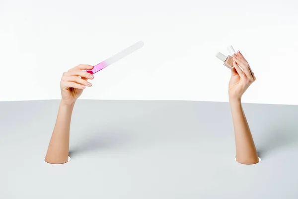 Partial view of woman holding nail file and polishes through holes on white — Stock Photo