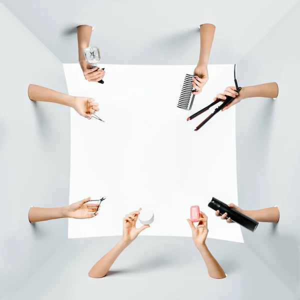 Cropped shot of women holding various beauty tools and products through holes on white — Stock Photo