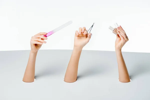 Cropped shot of women holding nail file, scissors and polishes through holes on white — Stock Photo