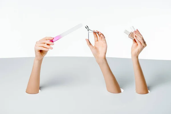 Abgeschnittene Aufnahme von Frauen, die Maniküre-Werkzeuge durch Löcher auf Weiß halten — Stockfoto