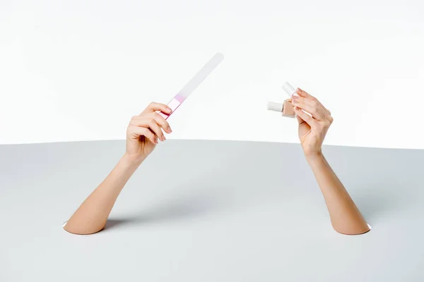 Cropped shot of woman holding nail file and polishes through holes on white — Stock Photo