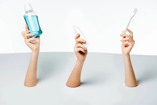 Abgeschnittene Aufnahme von Frauen, die Zahnpasta, Zahnbürste und Mundwasser durch Löcher auf weiß halten — Stockfoto