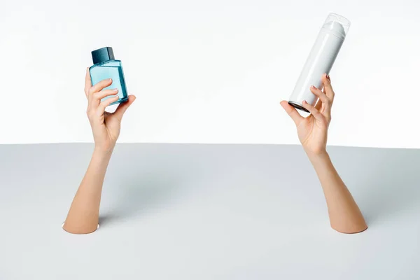 Cropped shot of woman holding containers with beauty products through holes on white — Stock Photo