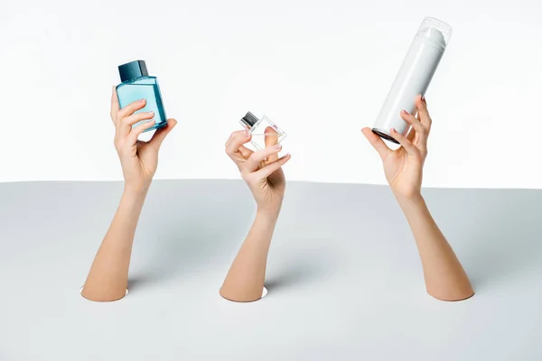 Tiro recortado de mãos femininas segurando perfumes através de buracos em branco — Fotografia de Stock