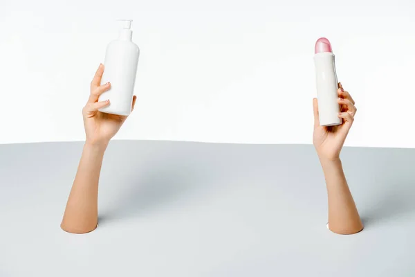 Partial view of woman holding beauty products through holes on white — Stock Photo
