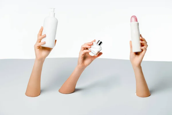 Partial view of women holding beauty products through holes on white — Stock Photo