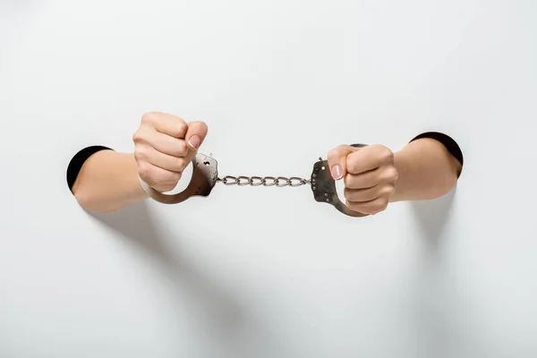 Cropped image of girl in handcuffs holding hands through holes on white — Stock Photo