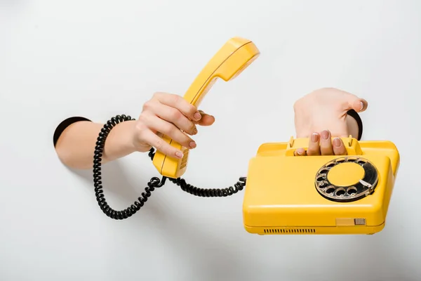 Cropped image of woman holding retro yellow stationary telephone through holes on white — Stock Photo