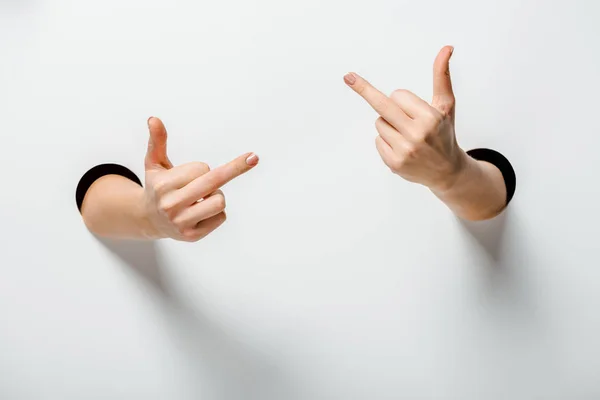 Cropped image of woman showing middle fingers through holes on white — Stock Photo