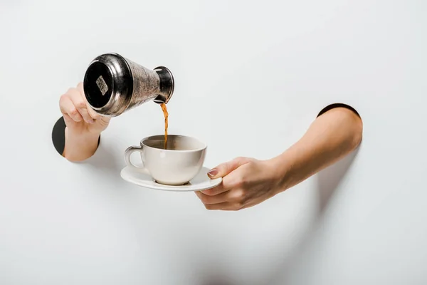 Cropped image of woman pouring coffee from cezve into cup through holes on white — Stock Photo