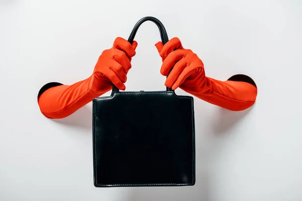 Cropped image of woman in red gloves holding black handbag through holes on white — Stock Photo