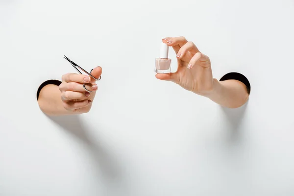 Image recadrée de femme tenant des ciseaux à ongles et vernis à ongles pour la manucure dans les trous sur blanc — Photo de stock