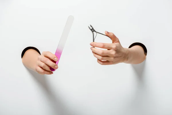 Обрезанное изображение женщины с ножницами для ногтей и пилкой для ногтей для маникюра в отверстиях на белом — стоковое фото