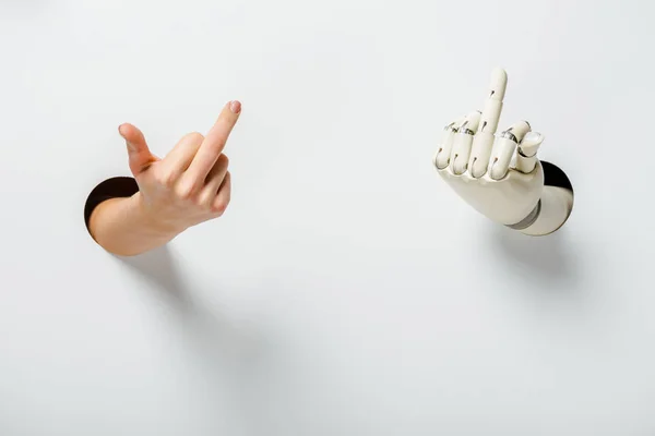 Cropped image of woman and robot showing middle fingers through holes on white — Stock Photo