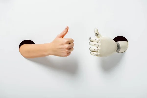 Cropped image of woman and robot showing thumbs up through holes on white — Stock Photo