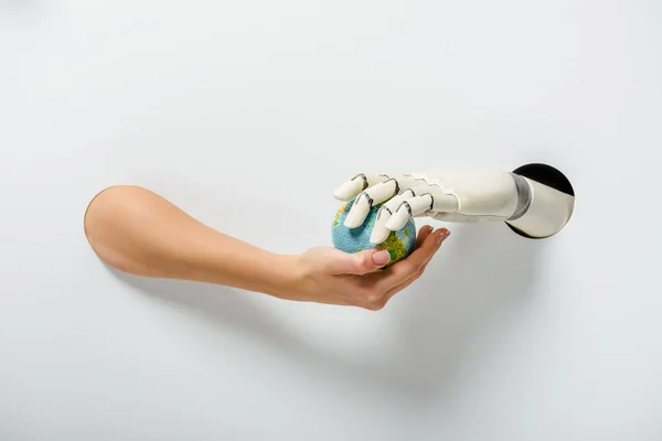 Cropped image of woman with hand prosthesis holding earth model through holes on white — Stock Photo