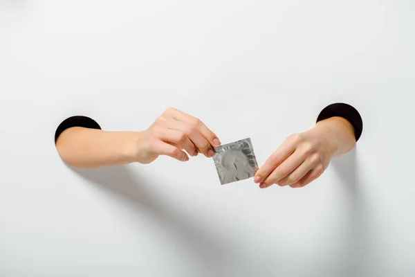 Cropped image of woman holding condom through holes on white — Stock Photo