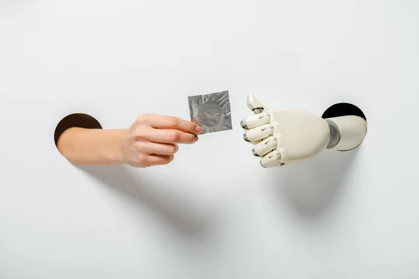 Abgeschnittenes Bild von Frau und Roboter, die Kondom durch Löcher auf Weiß halten — Stockfoto