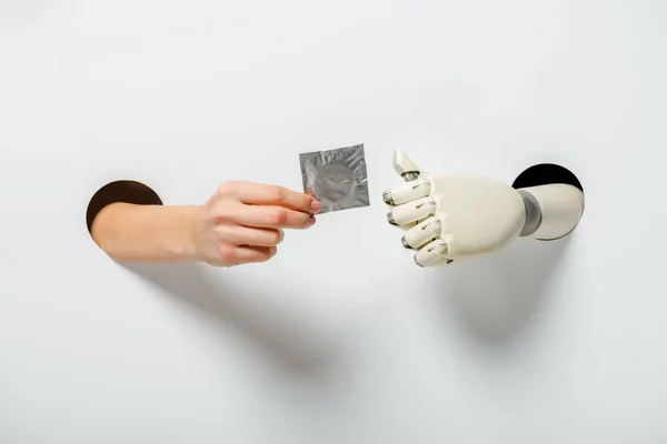 Cropped image of woman and robot holding condom through holes on white — Stock Photo