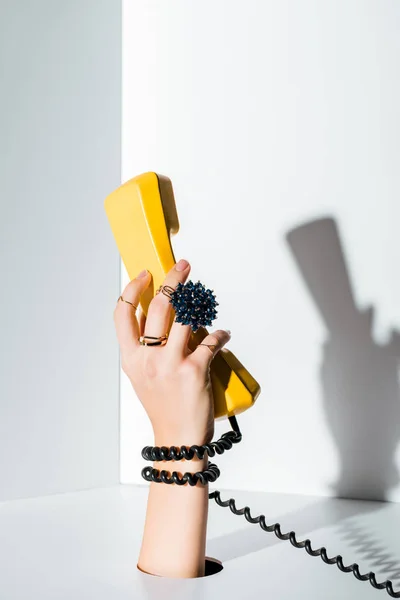 Immagine ritagliata della donna che tiene in mano il portatile giallo del telefono retrò attraverso il foro sul bianco — Foto stock