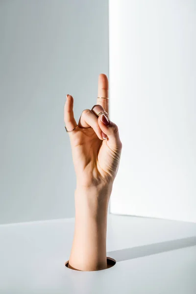 Image recadrée de la femme montrant signe de roche à travers le trou sur blanc — Photo de stock