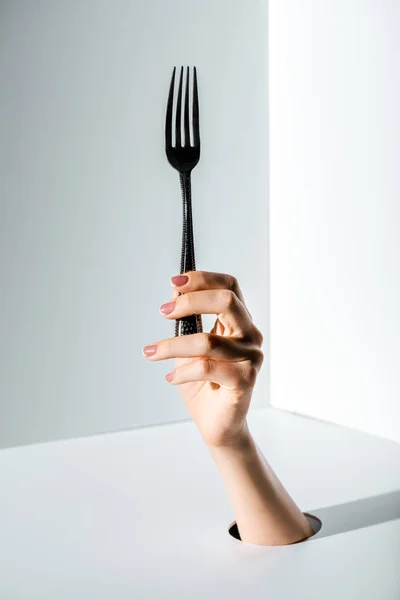 Immagine ritagliata della donna che tiene la forchetta in mano attraverso il foro sul bianco — Foto stock