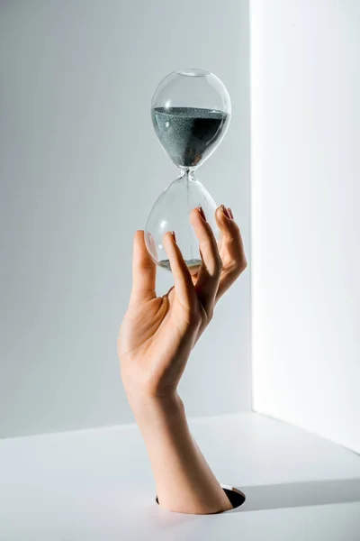 Cropped image of woman holding hourglass with grey sand in hand through hole on white — Stock Photo