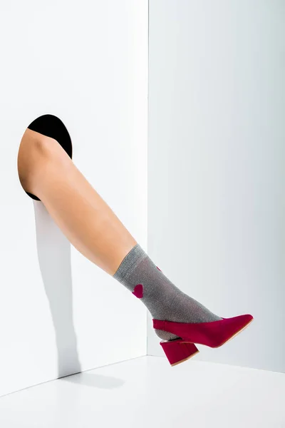 Ausschnittbild eines Mädchens, das Bein in stilvoller grauer Socke mit Herz und weinrotem High Heel in Loch auf weißem Grund zeigt — Stockfoto
