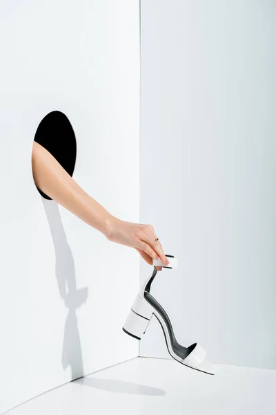 Cropped image of girl holding white high heel in hand through hole on white — Stock Photo