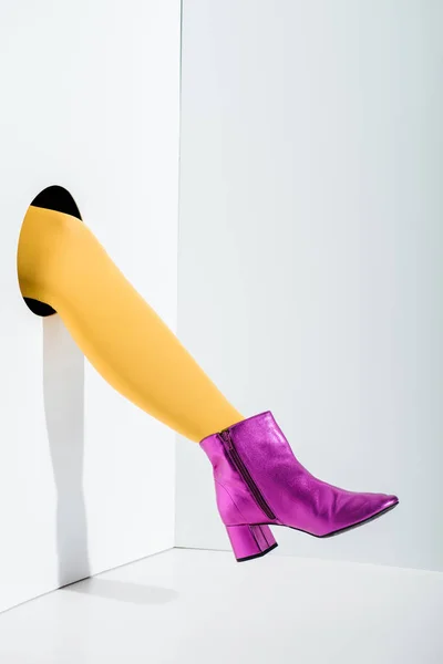 Cropped image of woman showing leg in bright yellow tights and ultra violet shoe in hole on white — Stock Photo
