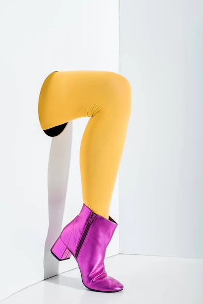 Cropped image of girl showing leg in bright yellow tights and trendy ultra violet shoe in hole on white — Stock Photo