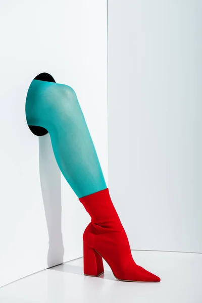 Cropped image of girl showing leg in turquoise tights and red shoe in hole on white — Stock Photo