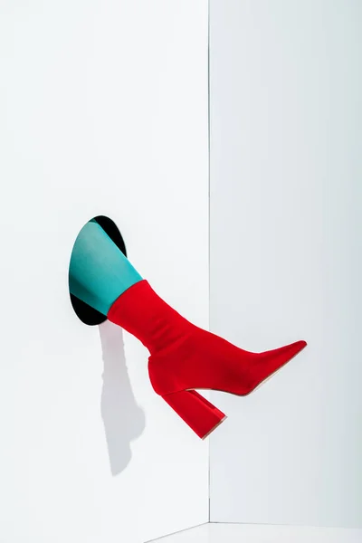 Cropped image of girl showing leg in bright turquoise tights and red shoe in hole on white — Stock Photo