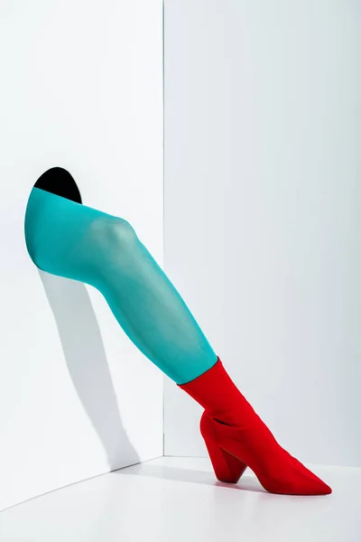 Cropped image of girl showing leg in stylish turquoise tights and red shoe in hole on white — Stock Photo