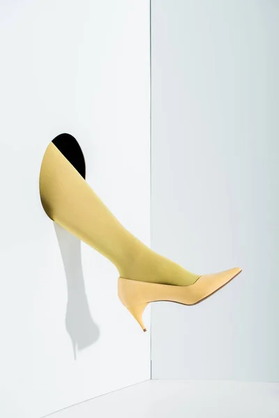 Abgeschnittenes Bild eines Mädchens, das Bein in stylischer gelber Strumpfhose und hohen Absatz in Loch auf weißem Grund zeigt — Stockfoto