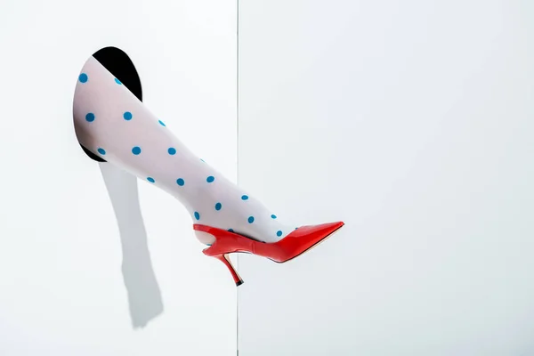 Image recadrée de la femme montrant la jambe en collants blancs avec des points bleus et rouge talon haut dans le trou sur blanc — Photo de stock