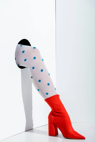Cropped image of girl showing leg in trendy white tights with blue dots and red shoe in hole on white — Stock Photo