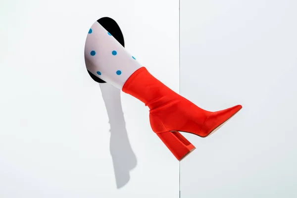 Cropped image of woman showing leg in white tights with blue dots and red shoe in hole on white — Stock Photo