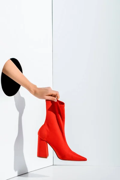 Abgeschnittenes Bild eines Mädchens mit rotem, stylischem High Heel in der Hand durch ein Loch auf weißem Grund — Stockfoto