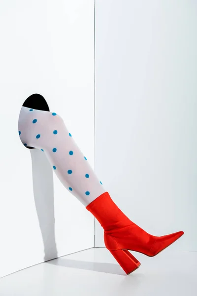 Cropped image of girl showing leg in stylish white tights with blue dots and red shoe in hole on white — Stock Photo