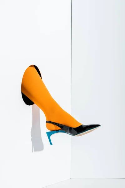 Обрізане зображення дівчини, що показує ногу в яскраво-помаранчевих колготках і чорний високий каблук в дірі на білому — стокове фото